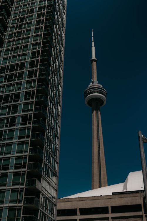 Free Stunning view of Toronto's CN Tower with adjacent high-rise building under a clear blue sky. Stock Photo