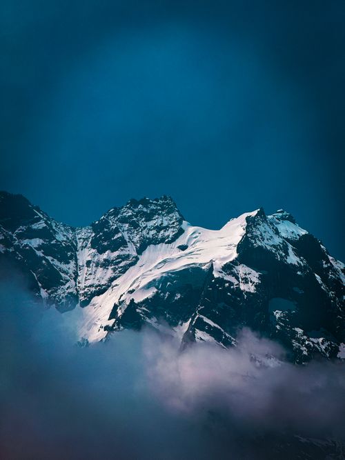 Free Stunning view of a snow-capped mountain peak emerging through mist at dusk with a deep blue sky. Stock Photo