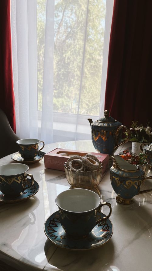 Free Charming afternoon tea setting with teacups, teapot, and treats by bright window light. Stock Photo