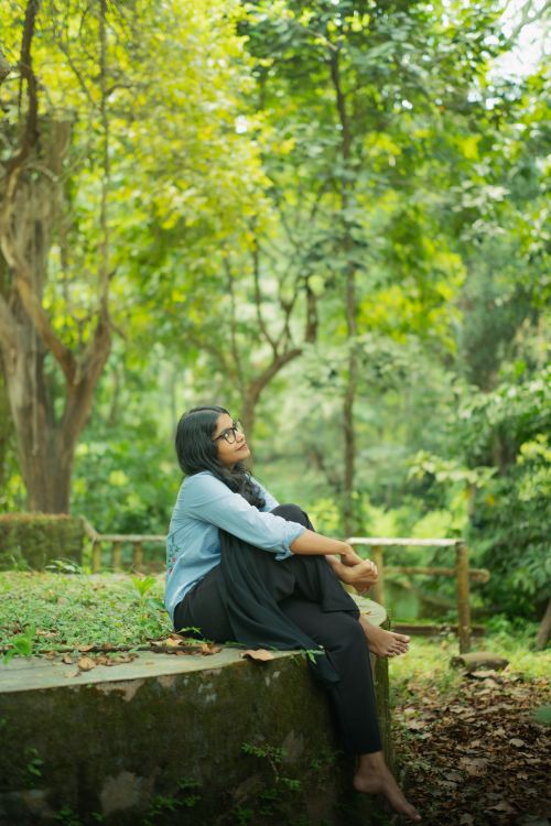Free A young woman enjoys a peaceful moment sitting in a lush, green forest, embodying serenity and connection with nature. Stock Photo