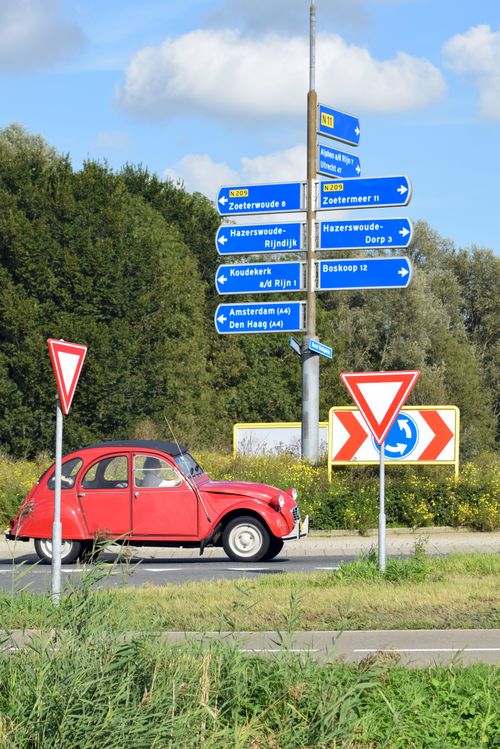 Free A red vintage car passing road signs in Alphen aan den Rijn, Netherlands. Stock Photo