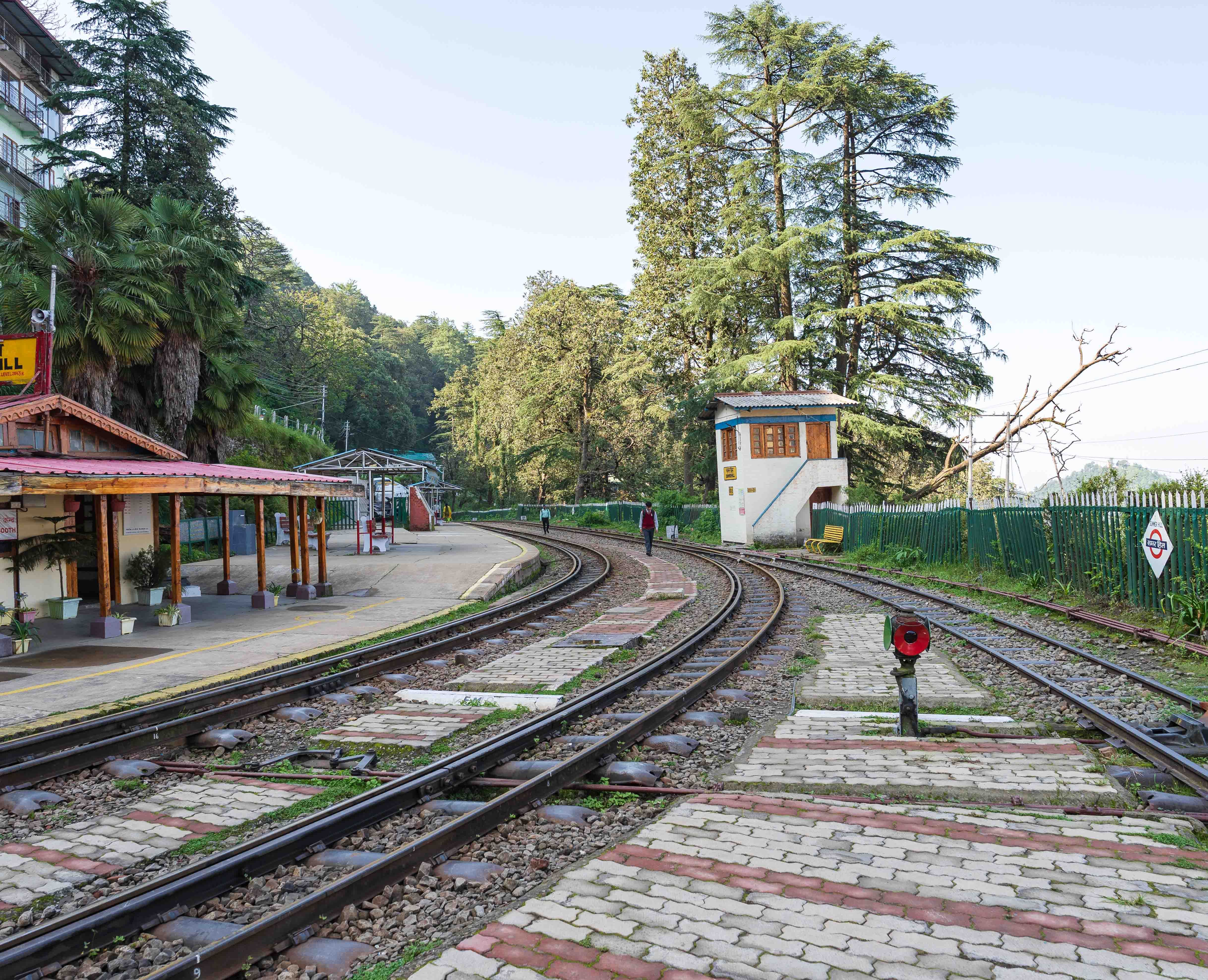 Charming railway station nestled in lush forest, capturing serene travel vibes with curved tracks and clear sky.