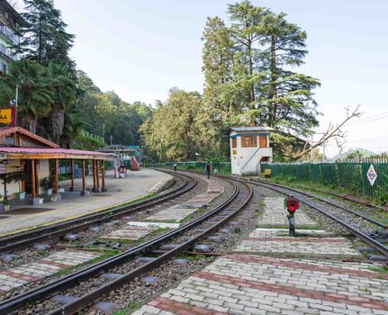Charming railway station nestled in lush forest, capturing serene travel vibes with curved tracks and clear sky.