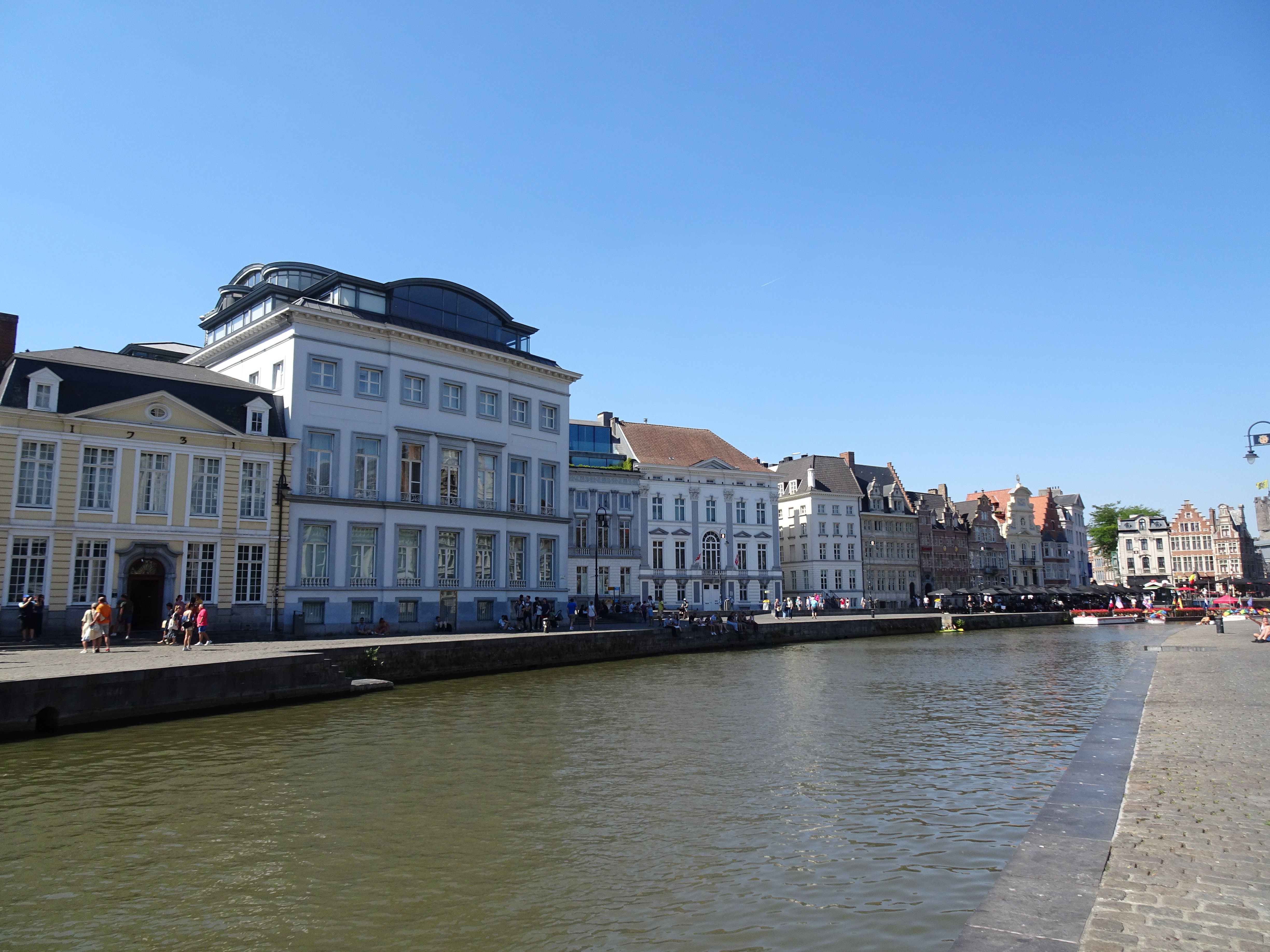 Charming view of medieval buildings along a canal in Ghent, Belgium, under a clear blue sky.