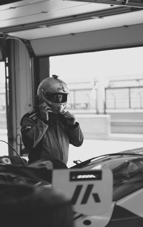 Free Monochrome image of a race car driver adjusting helmet inside a pit garage. Stock Photo