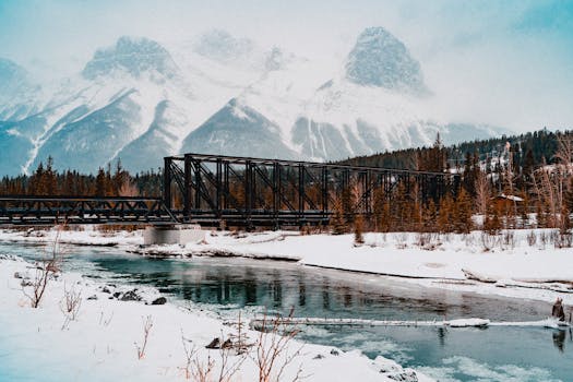 Stunning winter view of a snowy bridge with mountains in Canmore, Alberta.