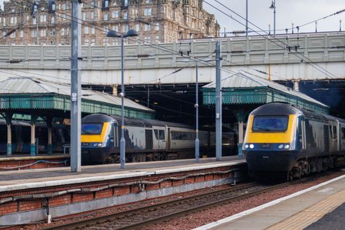 Free Trains arriving and departing Edinburgh Waverley Station with historic architecture visible above. Stock Photo