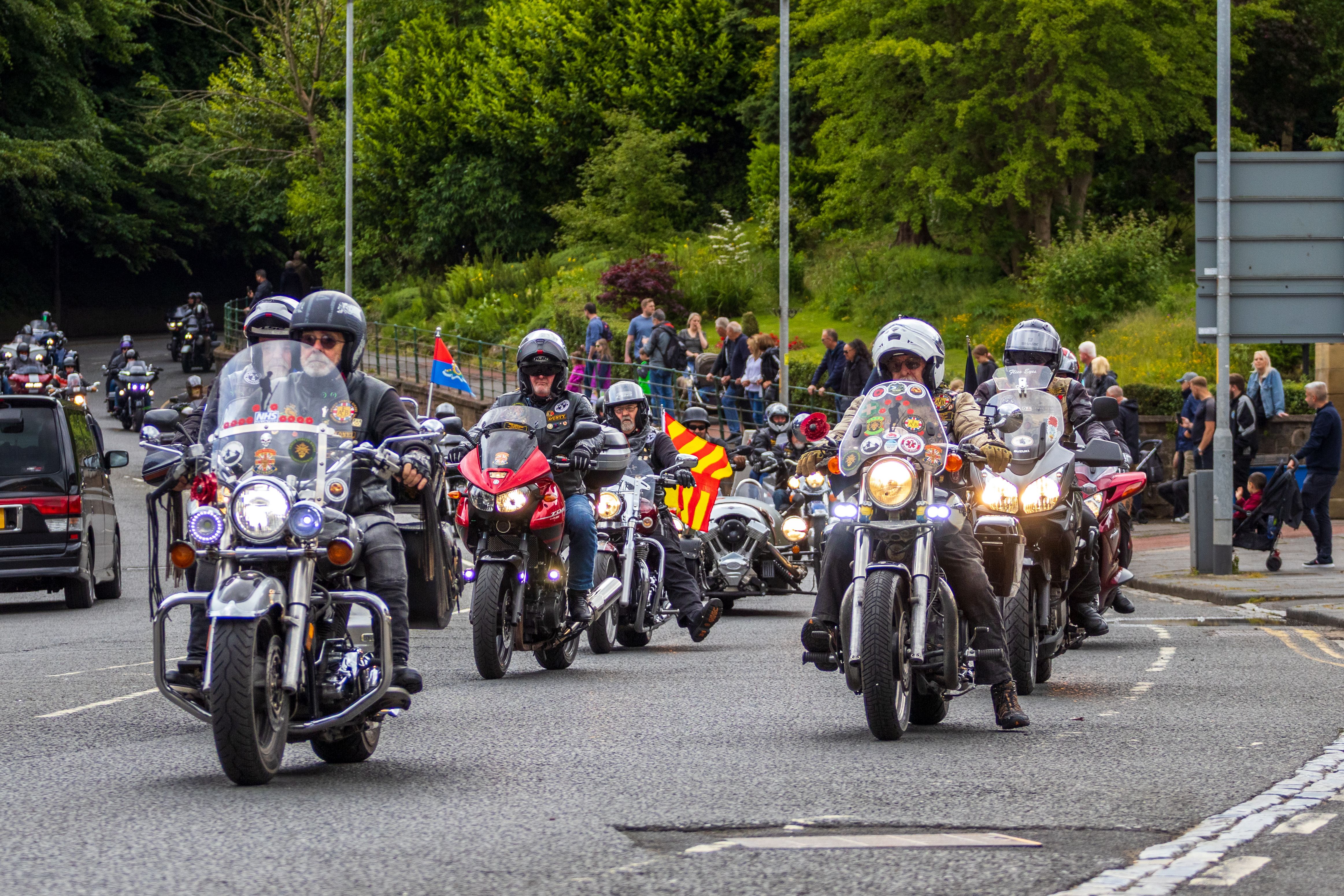 A vibrant motorcycle parade on a bustling street in Morpeth, England, featuring riders and spectators.