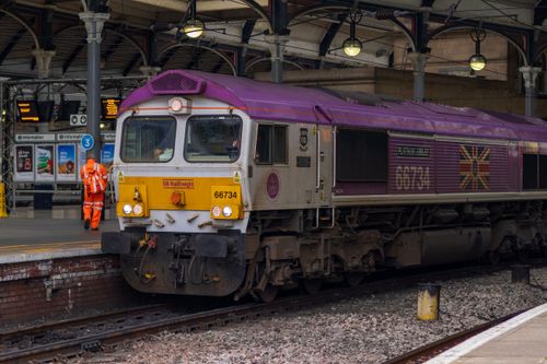 Free GB Railfreight locomotive 66734 at a station platform with worker nearby. Stock Photo