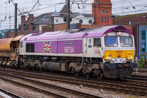 Free Colorful GB Railfreight train passing through urban area with red brick buildings. Stock Photo