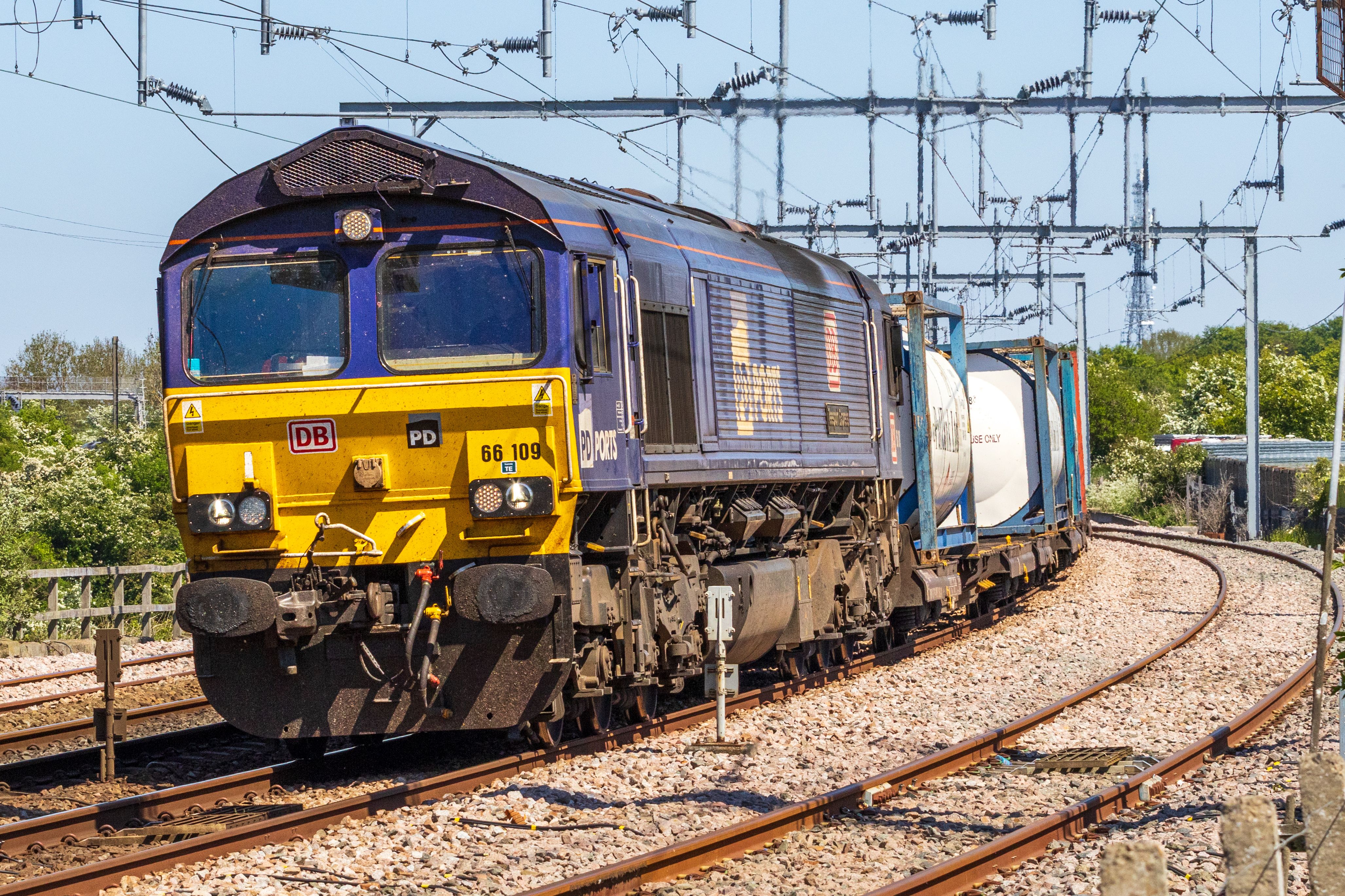 Row of vibrant cargo containers on train tracks under a clear blue sky.