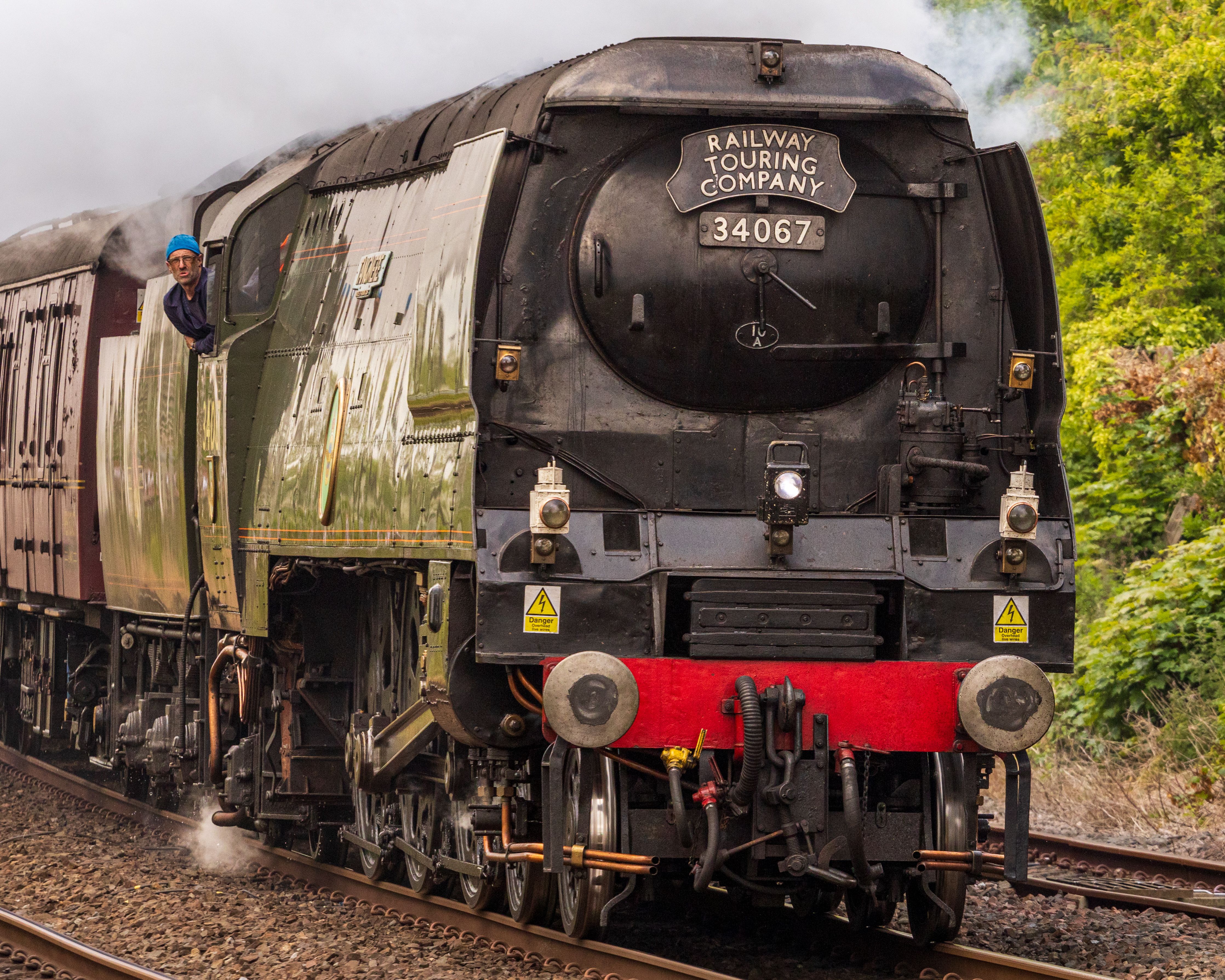 A classic steam locomotive with a visible driver on a railway track, showcasing vintage engineering.
