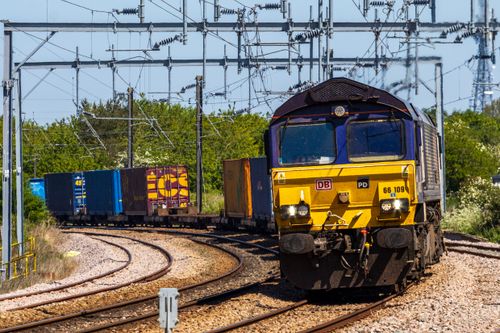 Free Colorful freight train moving along a curved railway track under power lines on a sunny day. Stock Photo