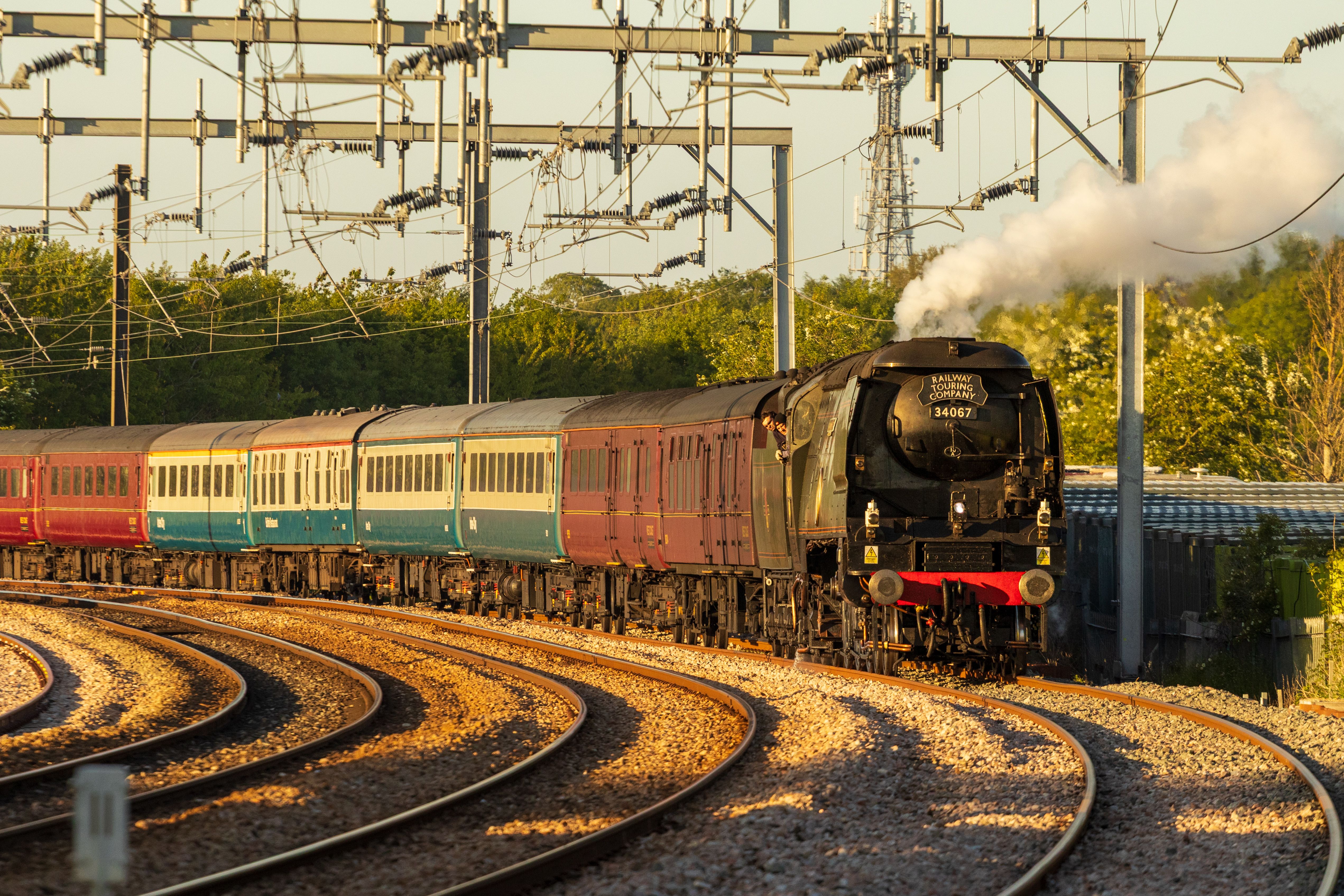 A vintage steam train travels on a curved track during sunset, emitting steam.