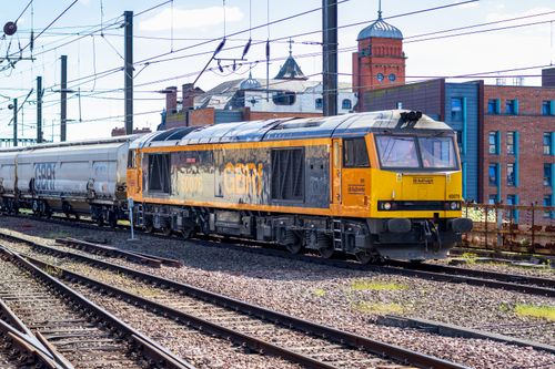 Free A bright yellow freight train on tracks surrounded by urban architecture under a sunny sky. Stock Photo