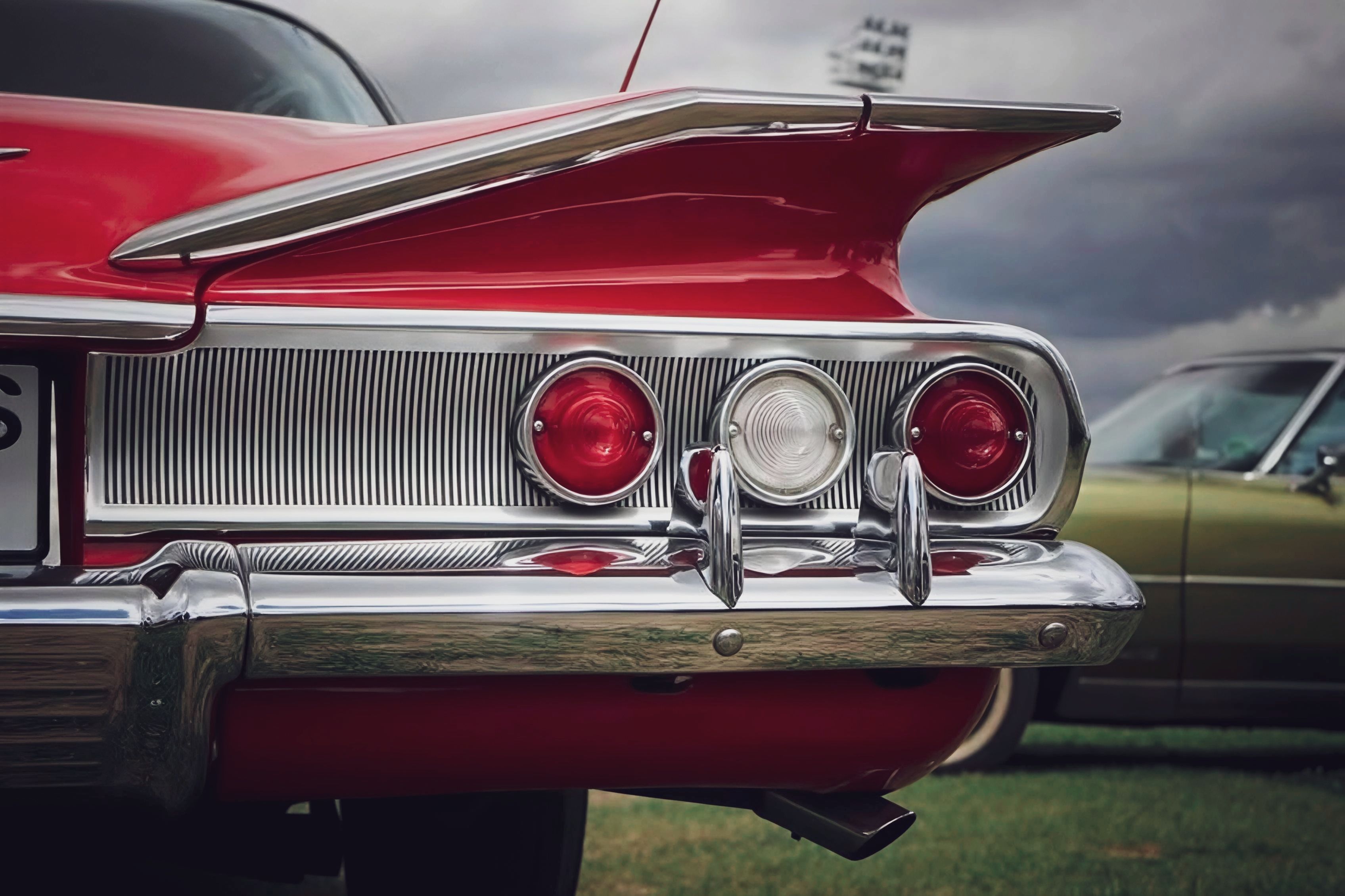 Close-up of a vintage red car tailfin and lights, showcasing retro chrome details.