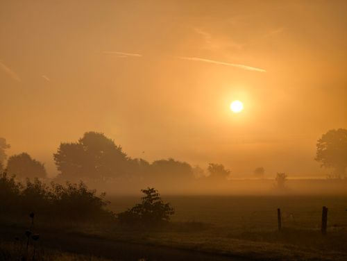 Free Beautiful sunrise illuminating a misty countryside landscape, creating a warm and tranquil scene. Stock Photo