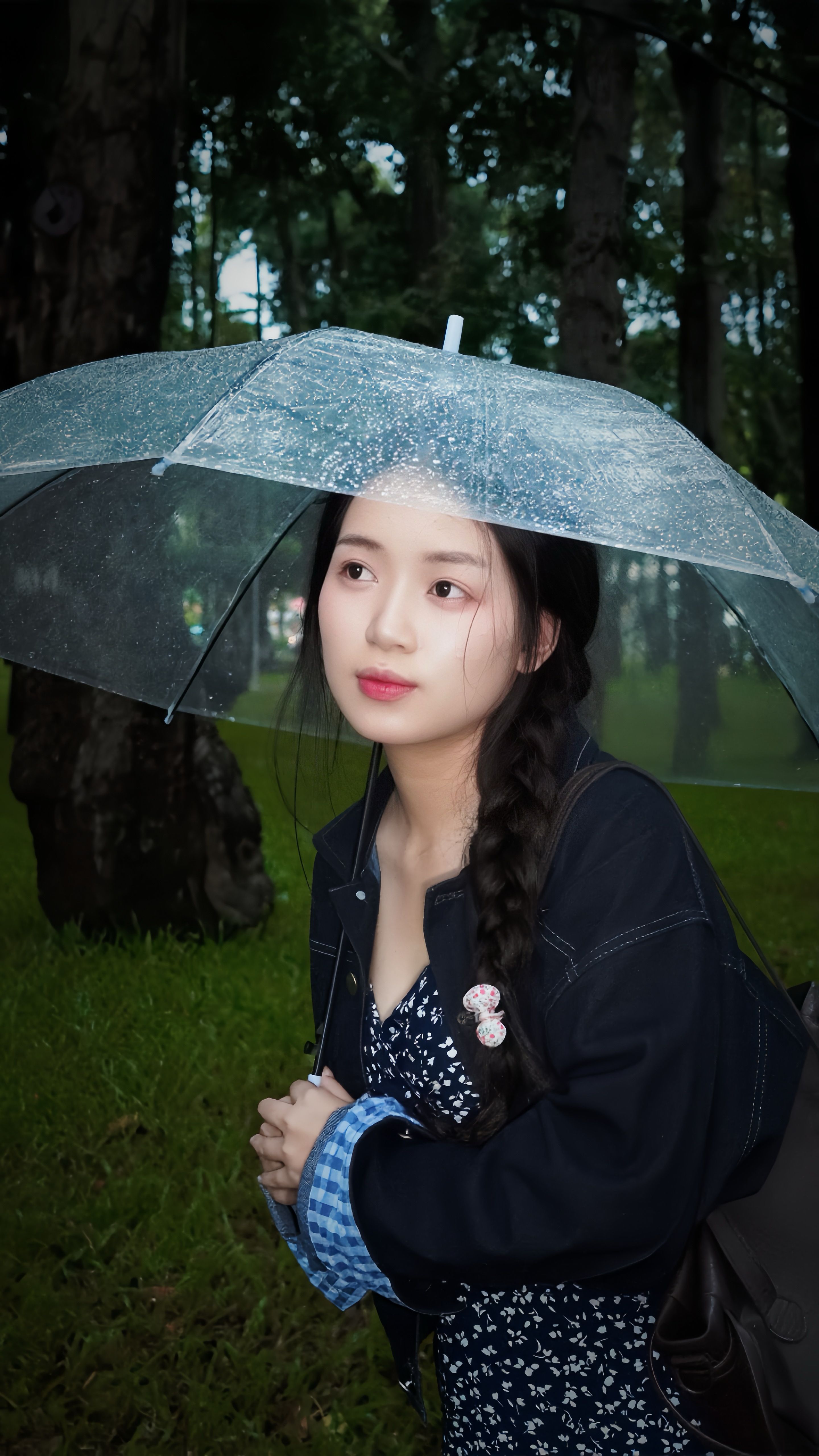 Portrait of a young woman under a clear umbrella in a lush forest setting.