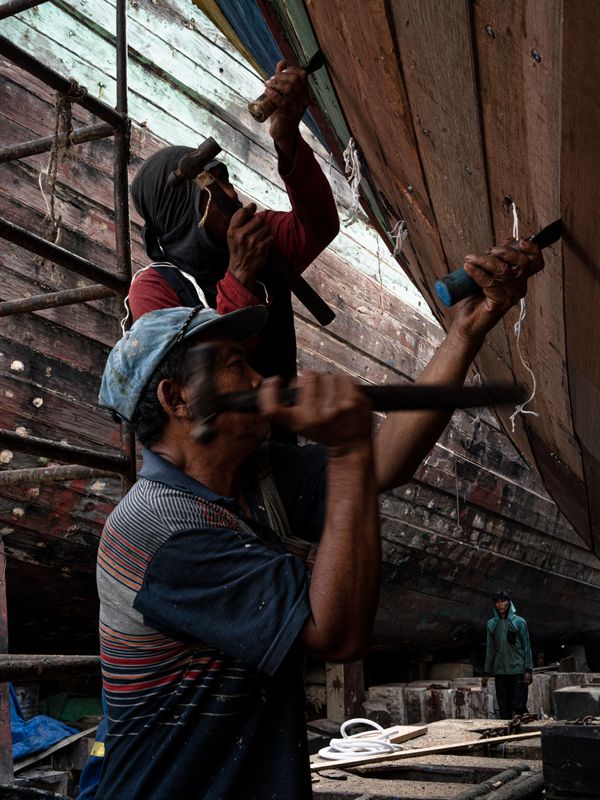 Two boatbuilders working on a large wooden hull