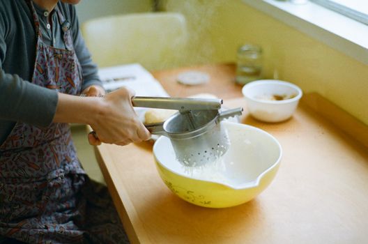 Person Sifting Flour Into a Yellow Bowl