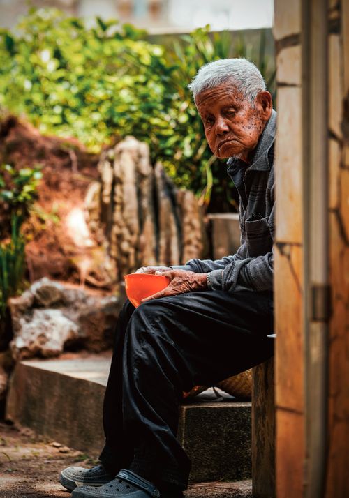 Free An elderly man seated with an orange bowl in an outdoor setting, reflecting peacefully. Stock Photo