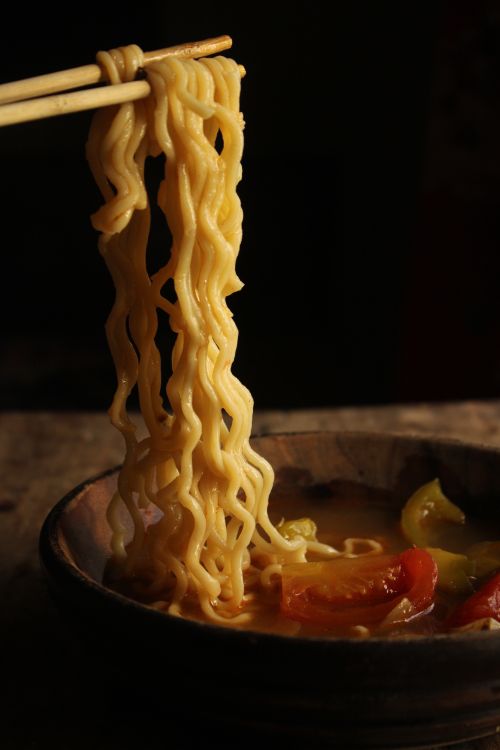 Free Close-up of ramen noodles lifted by chopsticks over a bowl, with a moody dark background. Stock Photo