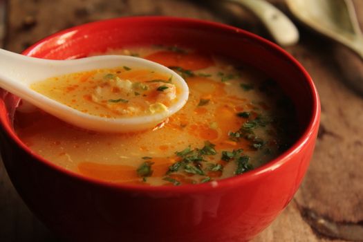 Close-up of a flavorful soup in a red bowl, garnished with fresh herbs.