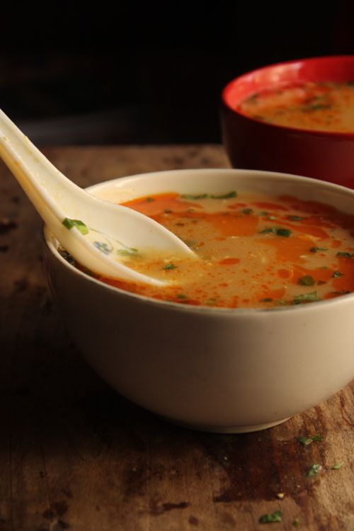 Free Tantalizing hot and sour soup served in a ceramic bowl with a spoon on a rustic table. Stock Photo