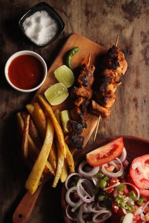 Free Close-up of grilled skewers served with fries, fresh salad, and sauces on a wooden platter. Stock Photo