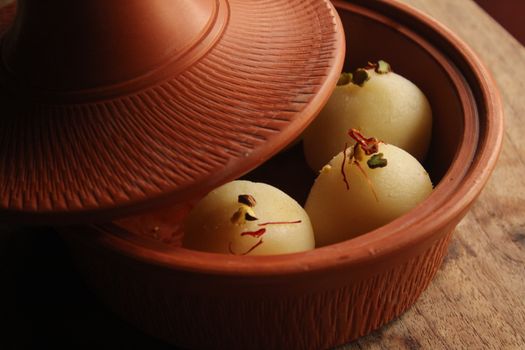 Close-up of Indian sweets in a traditional clay pot, garnished with nuts and saffron.