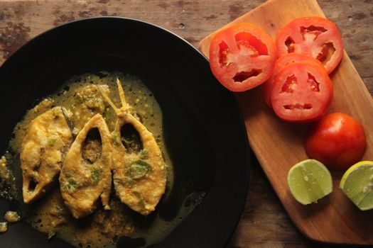 A savory fish curry served with fresh sliced tomatoes and lime, perfect for culinary delights.