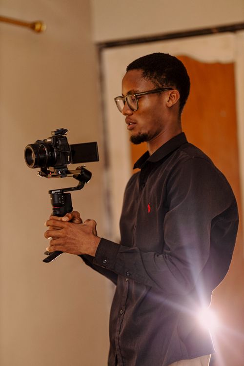Free Young man using a camera gimbal setup for video recording indoors, showcasing focus and technology. Stock Photo