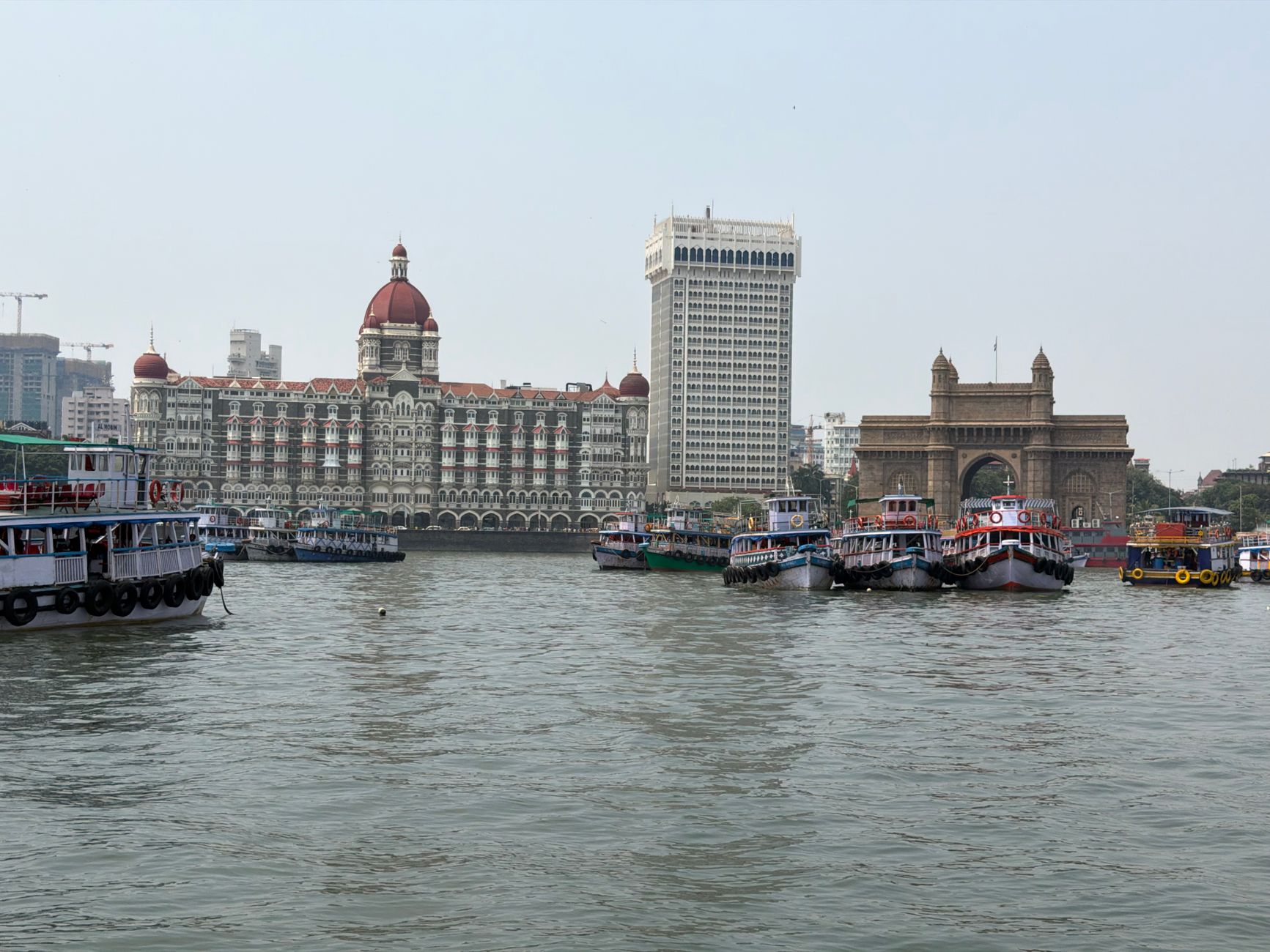 The Gateway of India and the Taj Mahal Palace hotel seen across Mumbai harbour, with boats moored in front
