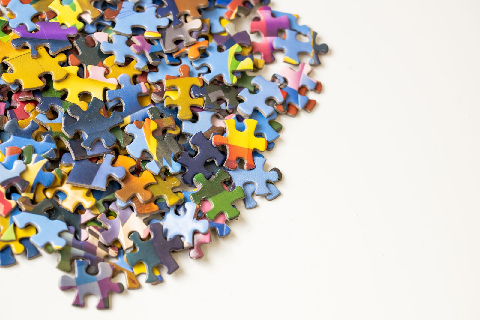 A pile of colorful jigsaw puzzle pieces scattered on a white background