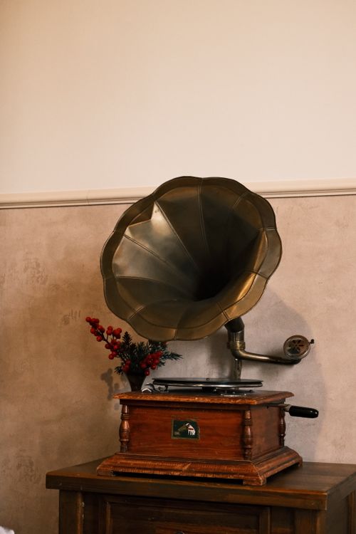 Free A classic brass gramophone atop a wooden table, accented by a red floral decoration against a neutral wall. Stock Photo