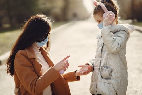 Caring mother spraying hands of daughter with antiseptic while walking in park