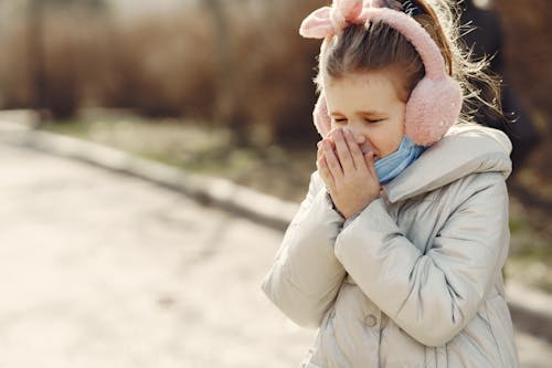 Little girl sneezing while walking in park