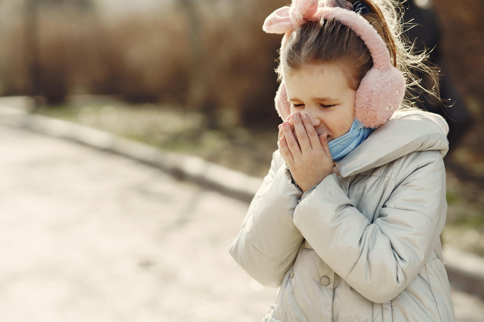 Petit enfant avec le masque du visage abaissé couvrant le visage par les mains tout en éternuant dans la rue