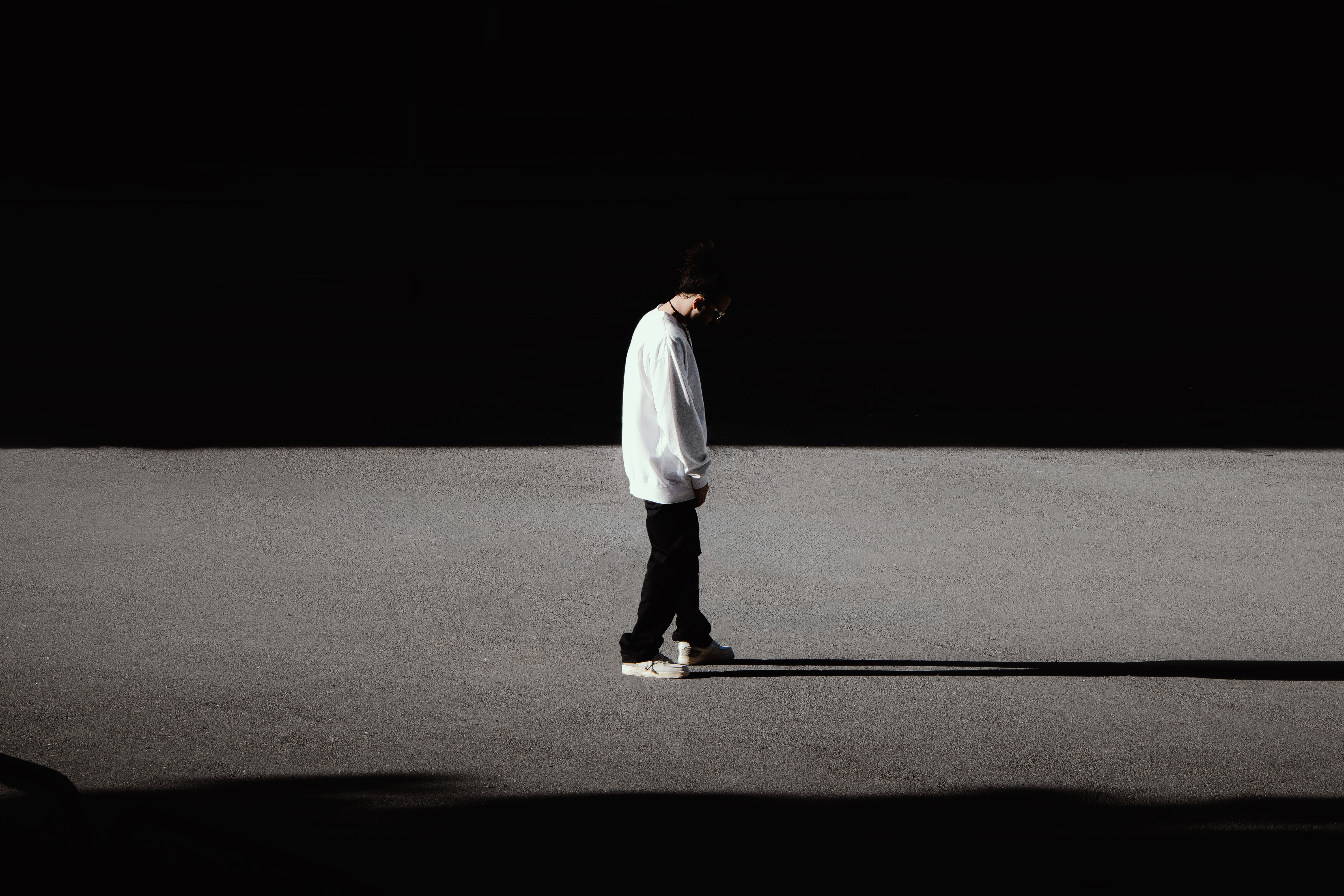A solitary person walking along a sunlit path surrounded by deep shadow contrast, creating a minimalist and dramatic visual effect.