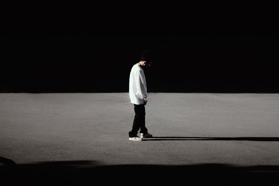 A solitary person walking along a sunlit path surrounded by deep shadow contrast, creating a minimalist and dramatic visual effect.