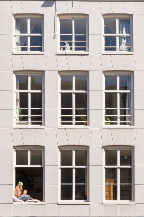 Free Serene afternoon scene with individuals relaxing by urban apartment windows. Stock Photo