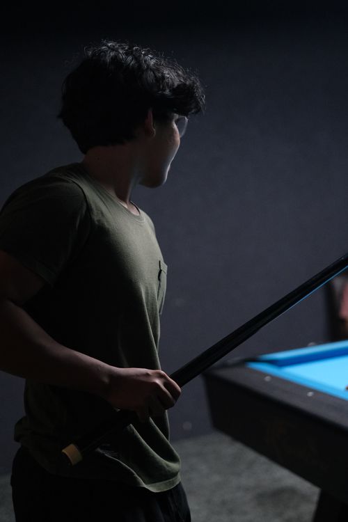 Free A young man holding a cue stick, focused on a billiard game in a dim setting. Stock Photo