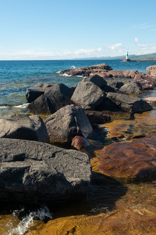 Free Idyllic view of a rocky shoreline with a distant lighthouse and vibrant blue waters in Grand Marais, Minnesota. Stock Photo