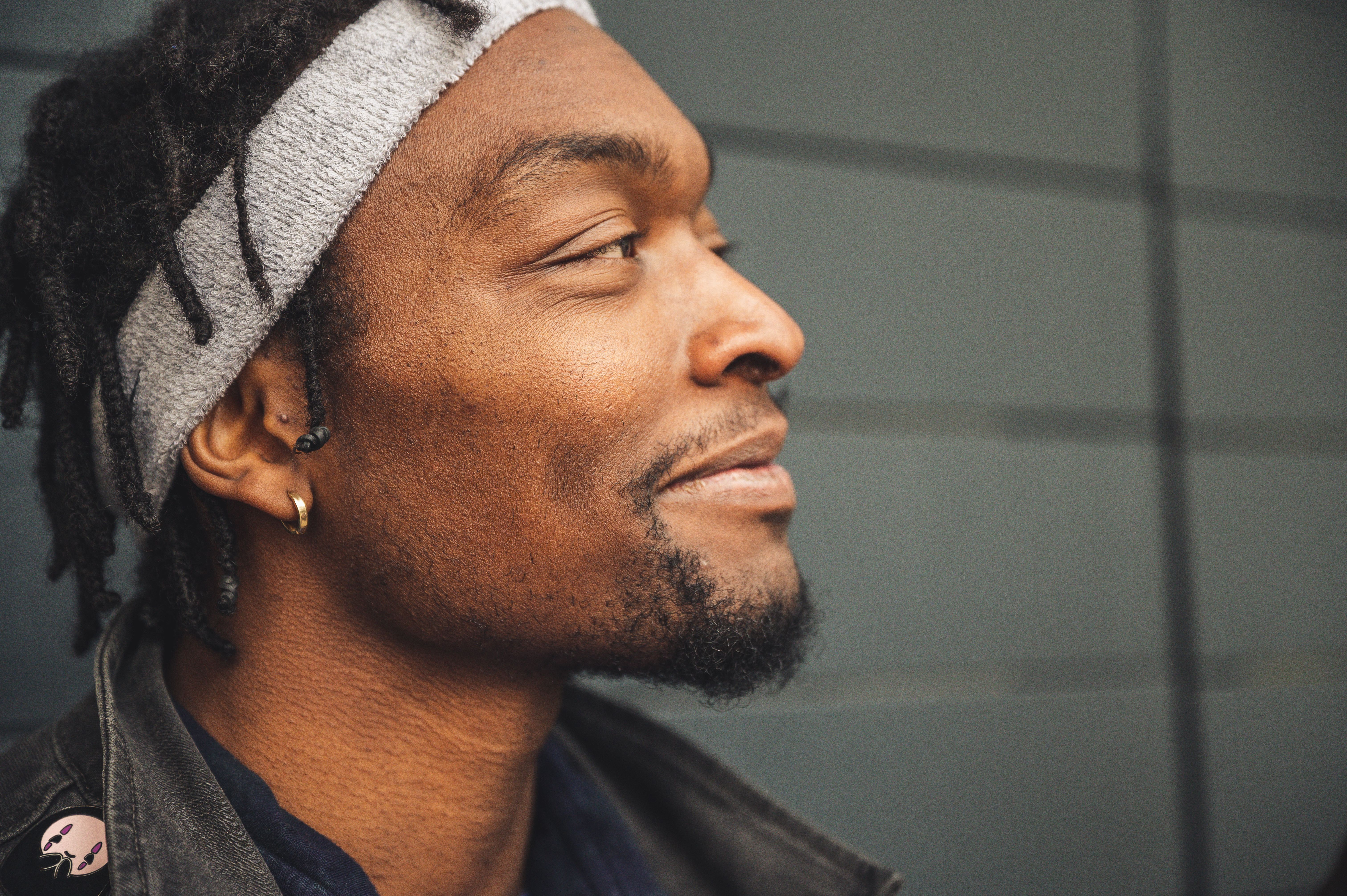 A close-up side view of a smiling man wearing a headband against a gray wall.