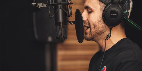 A young male musician singing in a professional recording studio with a microphone and headphones.