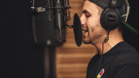 A young male musician singing in a professional recording studio with a microphone and headphones.