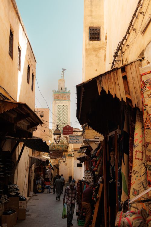 Free Lively alleyway in Fes with local shops lining both sides under a clear sky. Stock Photo