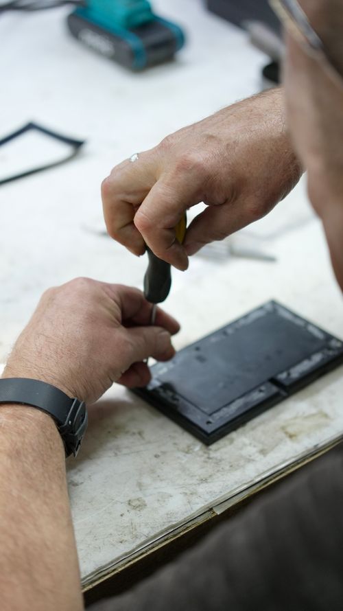 Free Technician using a screwdriver to repair an electronic device on a workbench. Stock Photo