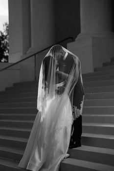 A bride and groom share a romantic kiss under a veil on elegant staircase.