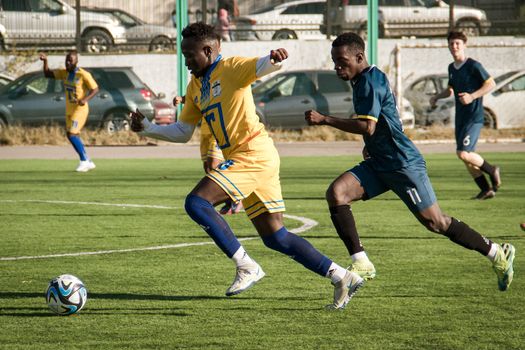 Soccer players in action during a competitive match on a sunny day in Almaty, Kazakhstan.